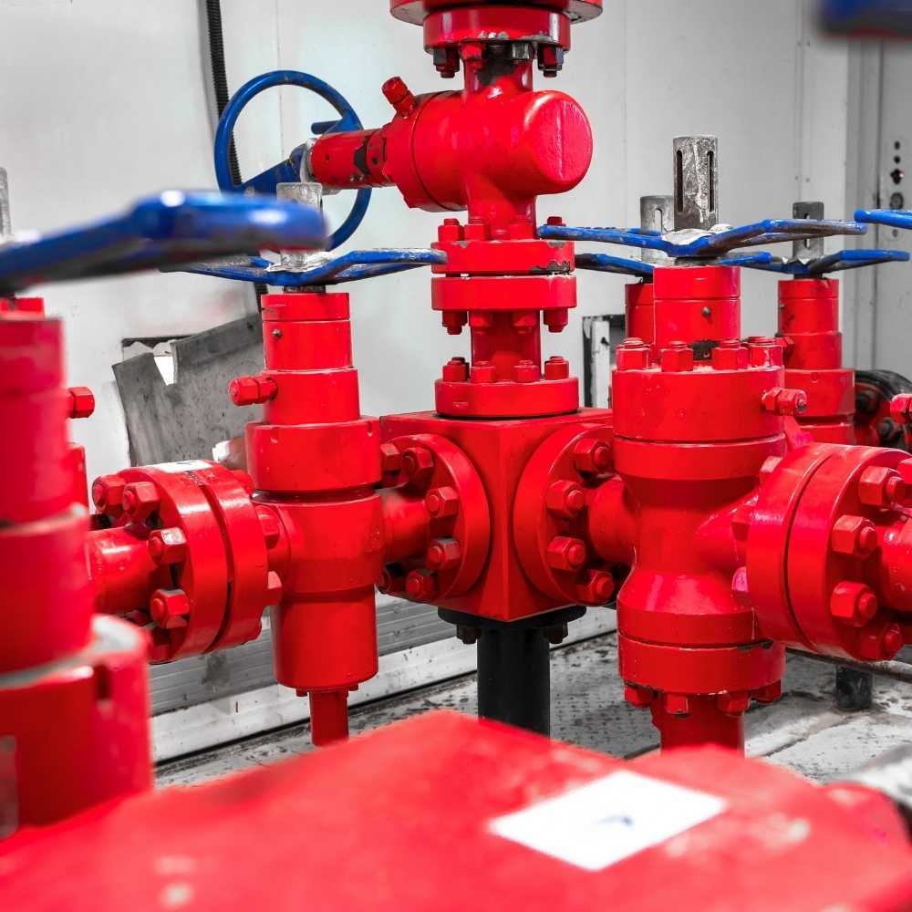 Untitled design - 2026-05-10T141329387 - rawatflowline.com Industrial red valve manifold with multiple bolted connections and blue handles in a mechanical room. (informative image)