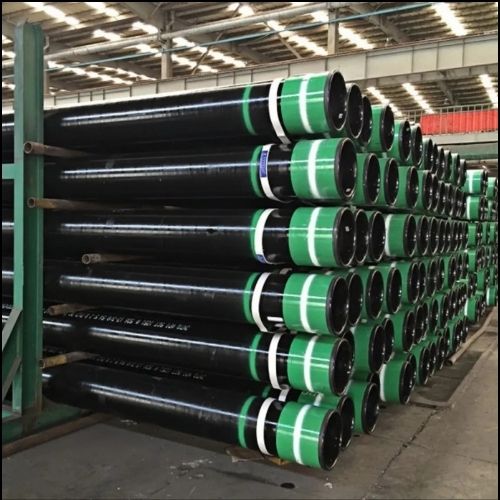 5 CT Rows of large black industrial pipes with green and white bands stacked on racks in a warehouse.